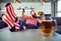 Thick funny man eating a burger sitting on the couch.