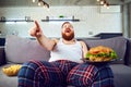 Thick funny man with a burger sitting on the couch.