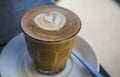 Thick glass tumbler with cappuccino and latte-art in the form heart. Ffresh coffee with milk. On a wooden table with saucer, spoon Royalty Free Stock Photo