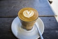 Thick glass tumbler with cappuccino and latte-art in the form heart. Ffresh coffee with milk. On a wooden table with saucer, spoon Royalty Free Stock Photo