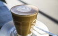 Thick glass tumbler with cappuccino and latte-art in the form heart. Ffresh coffee with milk. On a wooden table with saucer, spoon Royalty Free Stock Photo