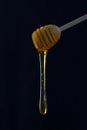 Thick golden honey dripping from a wooden spoon on black background