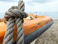 Thick grey rope tied to small orange boat Royalty Free Stock Photo