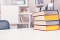 Thick old books with colorful covers lie in pile on white office table against backdrop of bookshelf. Royalty Free Stock Photo
