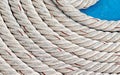 Thick powerful marine cable natural white weathered, a swirling row of coils lies on a blue deck