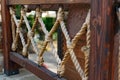 Thick rope ropes, intertwined crosswise, hang on wooden railings, decorative fence along the alley in the Park for recreation. Royalty Free Stock Photo