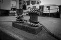 a thick rope is wound on a bollard in the harbor