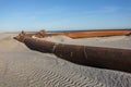 A thick rusty pipeline making a right angle turn on a sandy beach near the ocean at a beach replenishment site Royalty Free Stock Photo