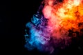 The thick smoke exhaled from the vape is highlighted by a blue-violet orange color like a rainbow against a black background Royalty Free Stock Photo