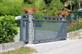 Thick strong metal sliding front yard driveway entrance doors mounted on stone column surrounded with wire fence and garden