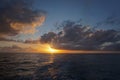 Thick white clouds over the horizon as the sun sets on the North Pacific Ocean