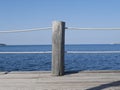 A thick white rope is attached to a massive wooden pole against the sea. Makeshift platform fence for sunbathing on the beach on a Royalty Free Stock Photo