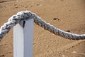 A thick white rope in a bow shape hangs on wooden poles on brown sea sand Royalty Free Stock Photo