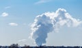 Thick white smoke from the nuclear plant in the distance against the bright blue Royalty Free Stock Photo