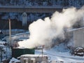 Thick white smoke over a green iron container on an industrial site against the background of a railway bridge in winter Royalty Free Stock Photo