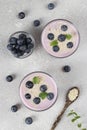 Thick yogurt with blueberries and sesame seeds in glasses, as well as in wooden spoon on gray background, Top view Royalty Free Stock Photo