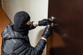 Thief in black mask trying to pick lock a door. House thief concept. Royalty Free Stock Photo