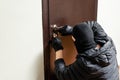 Thief in black mask trying to pick lock a door. House thief concept. Royalty Free Stock Photo