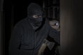 Thief with a flashlight and an ax in a mask with a slit for the eyes looking for prey in room Royalty Free Stock Photo