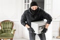 Thief looking at the camera with black balaclava stealing modern Electronic safe box. The burglar commits a crime in