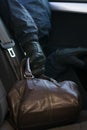 Thief`s hand steals brown leather bag from car backseat Royalty Free Stock Photo