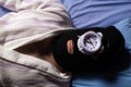 Thief of time, procrastination concept. A man in a balaclava lies and sleeps with an alarm clock on his face. Manage your time