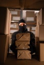 Thief wears gloves steal boxes of goods in a warehouse in the dark. Concept of problems with theft of postal parcels.