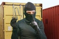 Thief at work - criminal man in black covered with balaclava mask holding unlocked padlock at shipping area break in storage