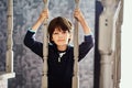 Slender, bored European boy, 7 years old, holds on to balusters of wooden staircase.