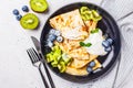 Thin crepes with curd cream, kiwi and blueberries in a black plate, top view