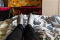 Thin female legs and feet in black pants and gray socks lie on the bed among colored fabric textiles