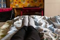 Thin female legs and feet in black pants and gray socks lie on the bed among colored fabric textiles