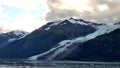 Thin Glacier between two mountains slowly gliding into the pacific ocean with a cloudy backdrop