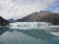 Thin Glacier between two mountains slowly gliding into the pacific ocean with a cloudy backdrop