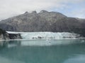 Thin Glacier between two mountains slowly gliding into the pacific ocean with a cloudy backdrop Royalty Free Stock Photo