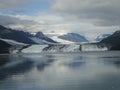 Thin Glacier between two mountains slowly gliding into the pacific ocean with a cloudy backdrop