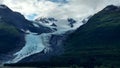 Thin Glacier between two mountains slowly gliding into the pacific ocean with a cloudy backdrop