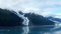 Thin Glacier between two mountains slowly gliding into the pacific ocean with a cloudy backdrop Royalty Free Stock Photo