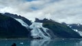 Thin Glacier between two mountains slowly gliding into the pacific ocean with a cloudy backdrop Royalty Free Stock Photo