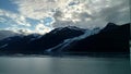 Thin Glacier between two mountains slowly gliding into the pacific ocean with a cloudy backdrop