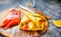 Thin pancakes with red fish on plate, top view.Crepes with filet salmon and cheese, red fish and green avocado on white plate over