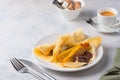 Thin pancakes stuffed with caramelized bananas and chocolate spread on a white plate against a light concrete background. Royalty Free Stock Photo