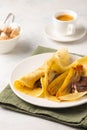 Thin pancakes stuffed with caramelized bananas and chocolate spread on a white plate against a light concrete background. Royalty Free Stock Photo