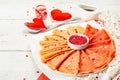 Thin red crepes or pancakes with raspberry sugar and sweet hearts pastry topping