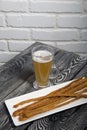 Thin sausages for beer. On a rectangular plate. Next to it is a glass of wheat beer. Background from pine boards. Close-up Royalty Free Stock Photo