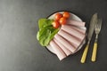 Thin slices of ham rolled on plate with fresh vegetables, dark background. Breakfast food, ingredient for sandwich. Flat lay food Royalty Free Stock Photo