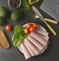 Thin slices of ham rolled on plate with fresh vegetables, dark background. Breakfast food, ingredient for sandwich. Flat lay food Royalty Free Stock Photo