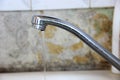 a thin stream of water flows from the tap, silver colored kitchen faucet on old wall background