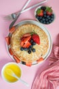 Thin traditional Russian pancakes on a trendy pink background with berries and honey. Vertical photo, top view Royalty Free Stock Photo