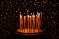 Thin yellow candles burning on the black background with glitter lights